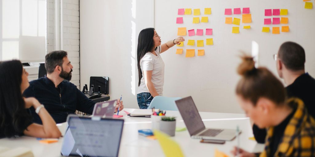 A team of professionals engaged in a collaborative meeting, with one person leading a brainstorming session using colorful sticky notes on a whiteboard. The image represents strategic planning, teamwork, and innovation in a modern workspace. It aligns with ProducifyX’s approach to fostering collaboration and creativity to attract top talent and streamline recruitment processes.
